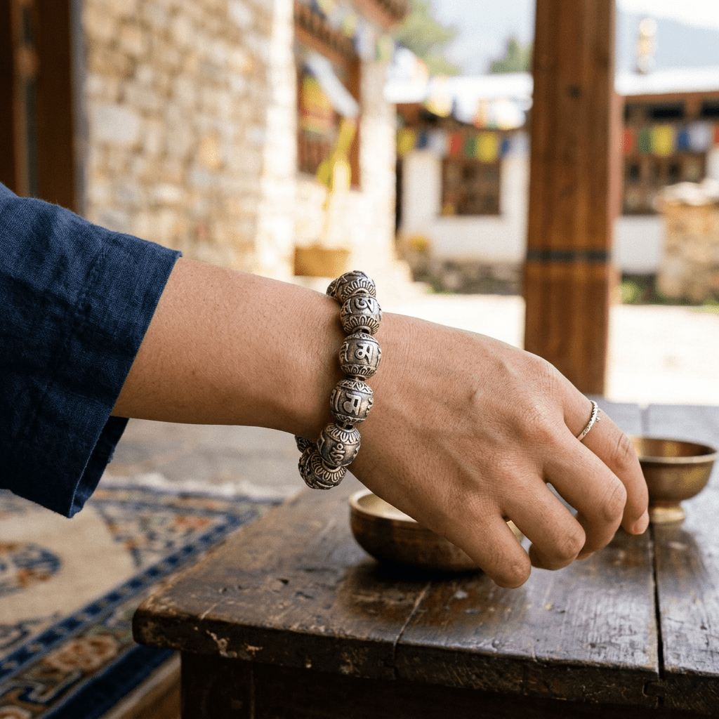 Hand wearing engraved meditation beads beside brass bowls on a wooden table